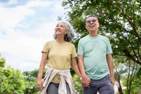 Glasses old man smiling and holding hand with old woman while walking together after exercise in park
