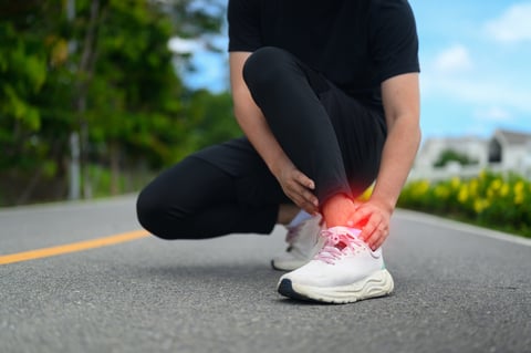 A runner crouches on a road clutching an injured ankle with a red glow indicating pain