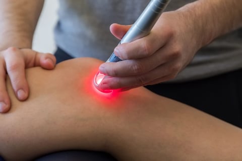 Person using a handheld red light laser device on another persons arm for therapeutic treatment